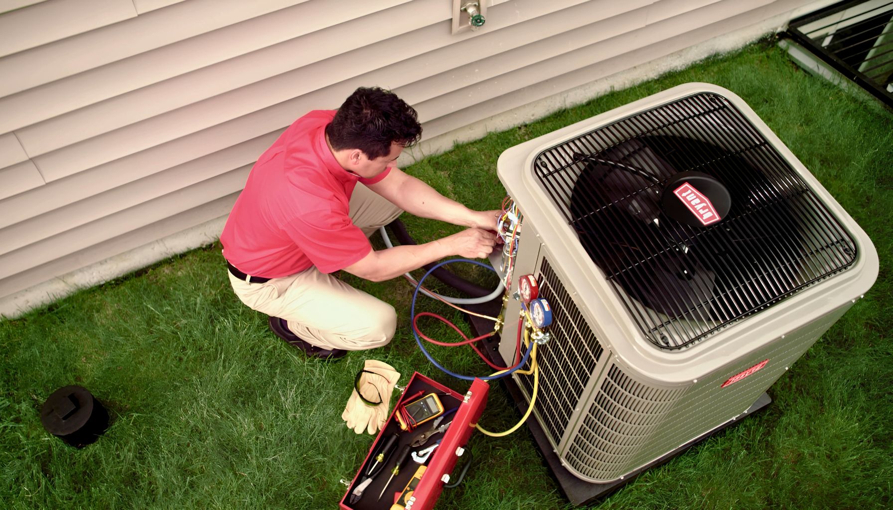 A technician wearing gloves services an outdoor bryant air conditioners ac unit, surrounded by tools on the grass, with a house in the background.