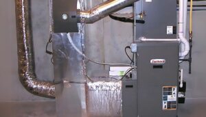 A modern furnace with shiny ductwork, connected pipes, and safety labels sits in a gray utility room, highlighting the importance of energy efficiency and understanding furnace replacement costs.